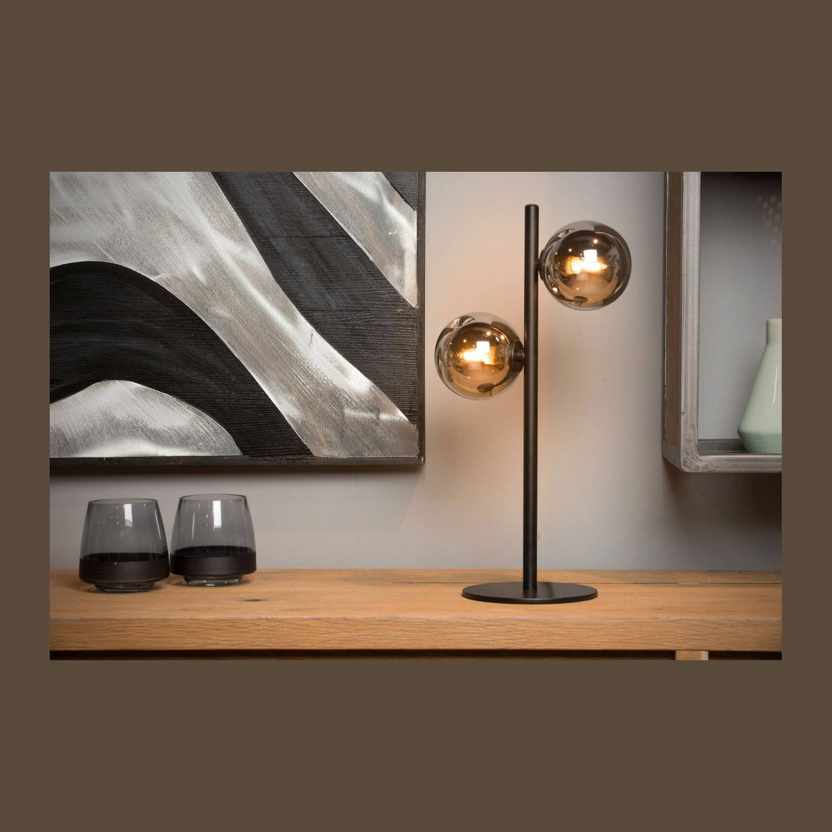 Lampe à poser noire à deux globes fumés sur un meuble en bois