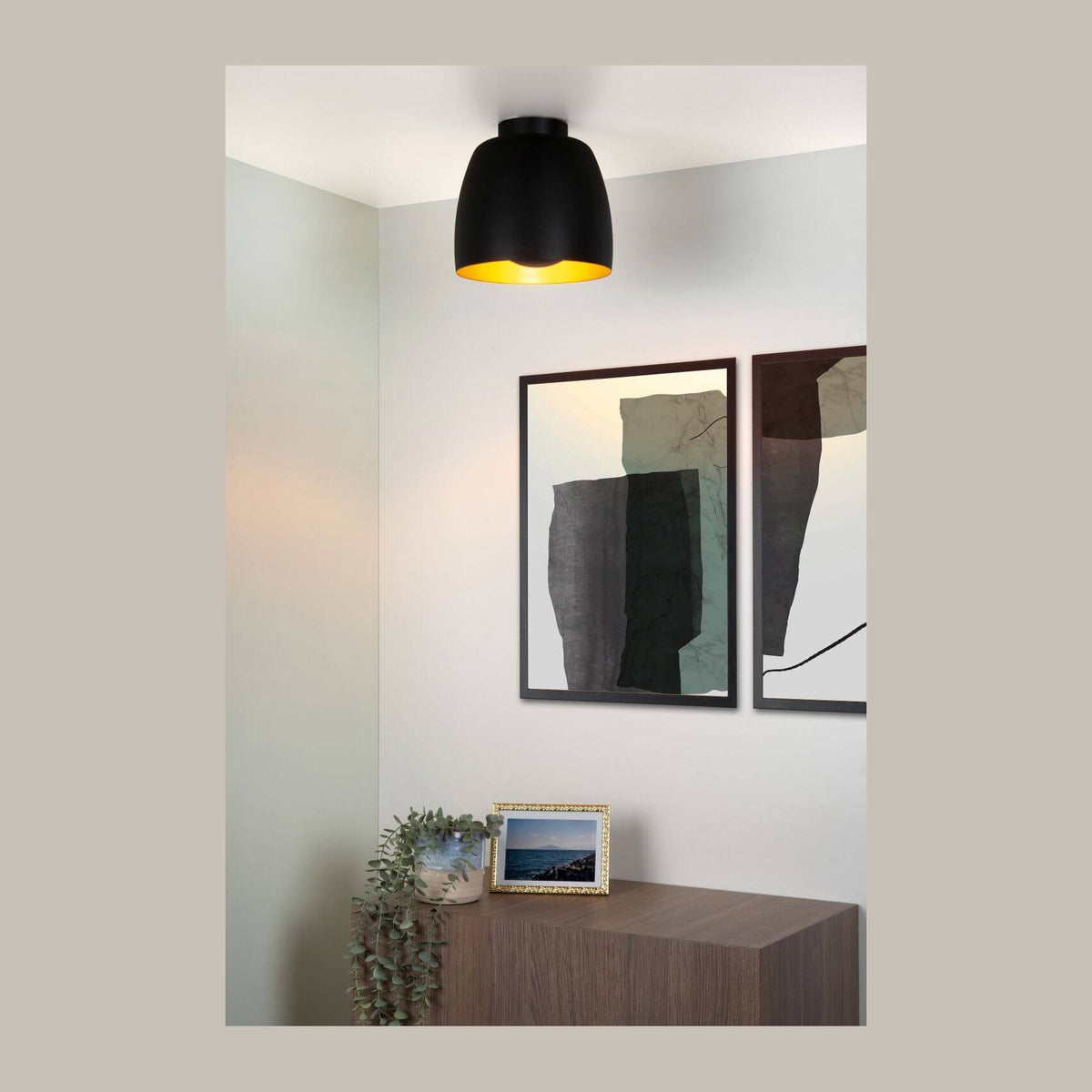 Plafonnier noir et doré éclairant un coin salon avec meuble, cadre photo et tableau.