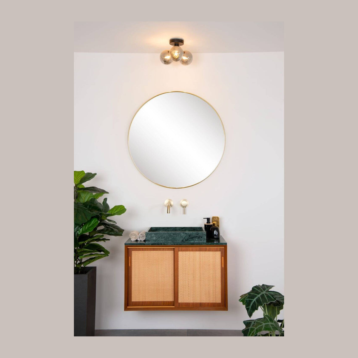 Plafonnier à trois globes en verre fumé au-dessus d'un miroir rond dans une salle de bain.