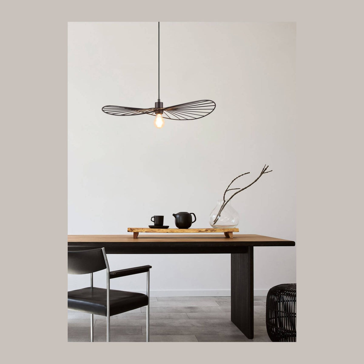 Suspension noire suspendue au-dessus d'une table en bois, avec chaise et vase décoratif.