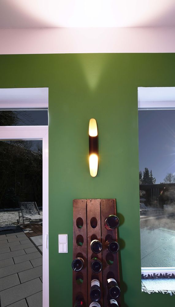 Applique allumée fixée sur un mur vert, au-dessus d'un casier à bouteilles.