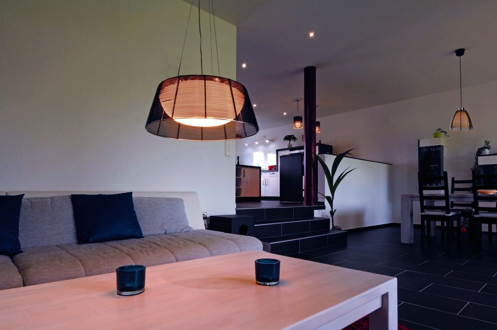 Mise en ambiance dans un salon, suspension noire éclairée au-dessus d’une table basse.