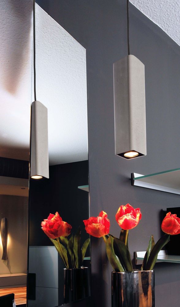 Deux suspensions en béton allumées dans un intérieur, avec miroir et tulipes rouges.