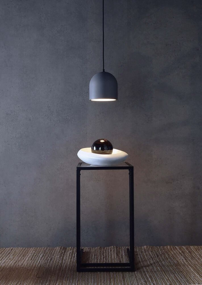 Mise en ambiance : suspension allumée au-dessus d'une table, mur béton et sol tissé.