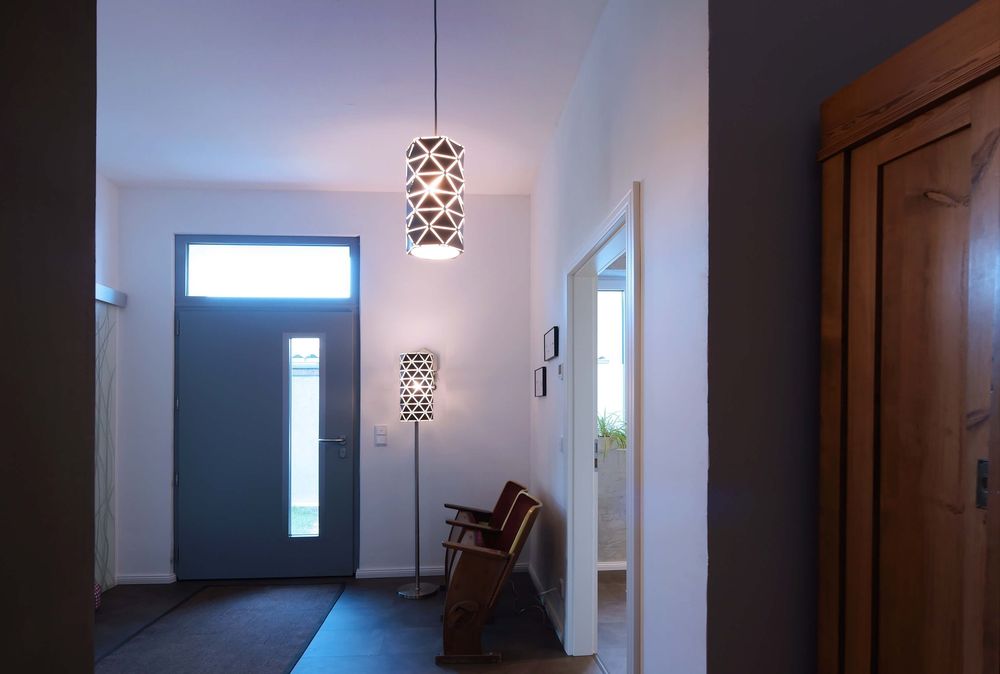 Mise en ambiance dans une entrée, lampadaire allumé près d’une porte et d’un fauteuil.