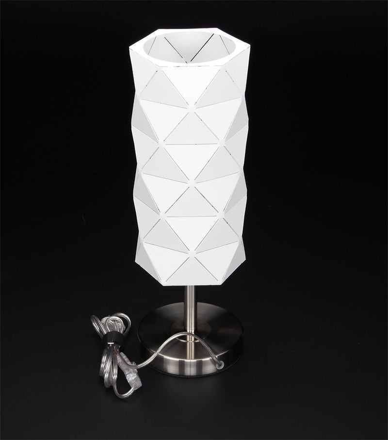 Lampe blanche de face sur fond noir, câble d'alimentation enroulé au pied de la base.