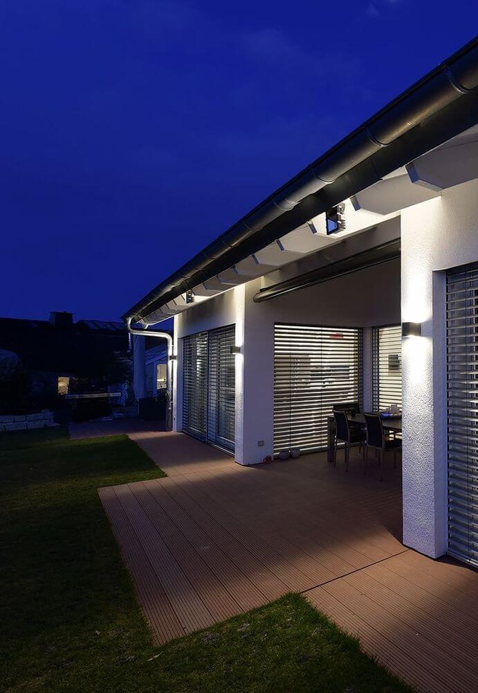 Applique murale allumée sur un pilier de terrasse, éclairant le plancher bois la nuit