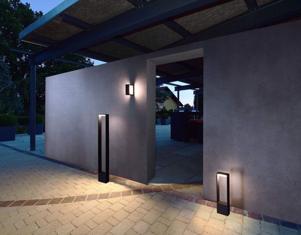 Mise en ambiance nocturne : deux lampadaires anthracite éclairent une allée pavée.