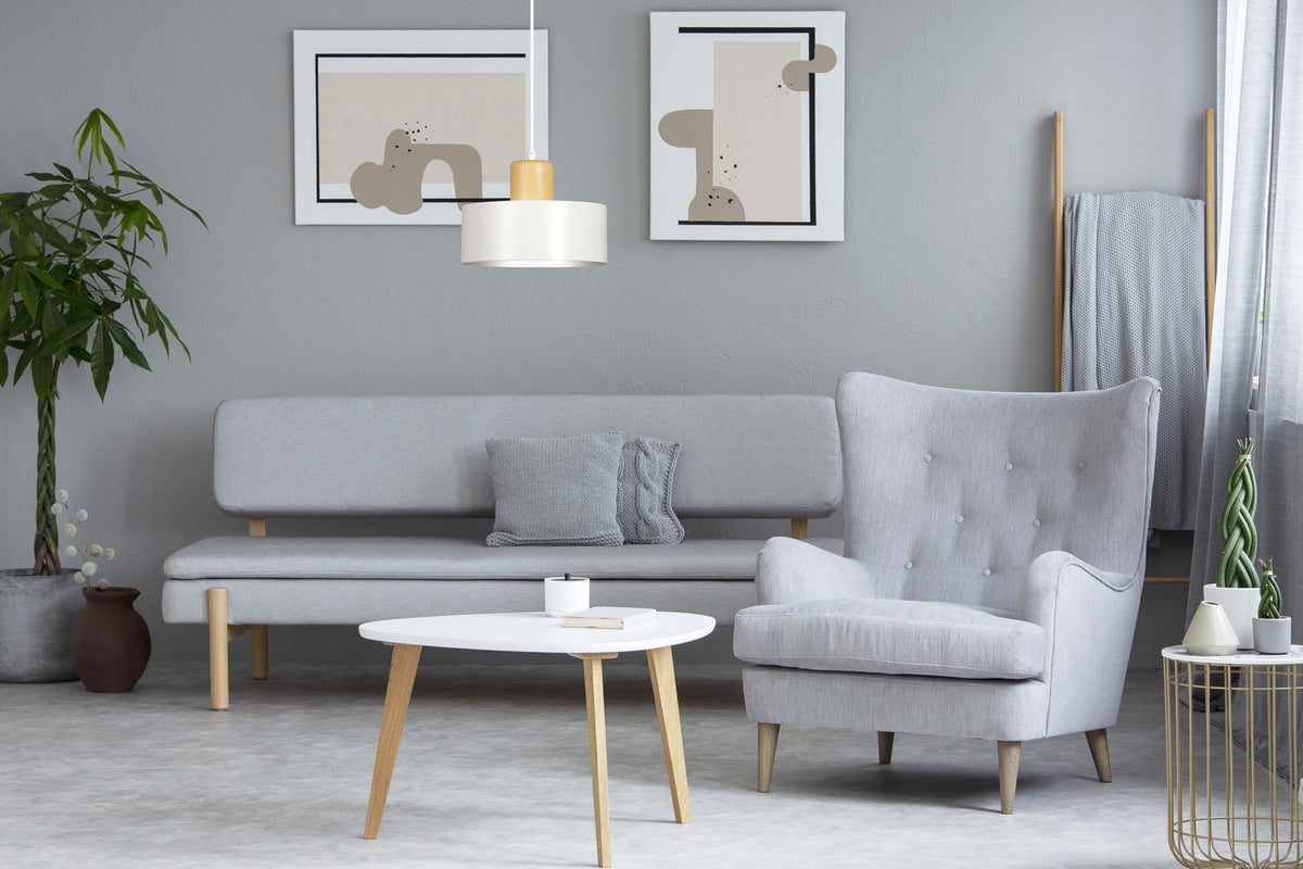 Suspension allumée au-dessus d’un salon gris clair avec canapé, fauteuil et table basse.