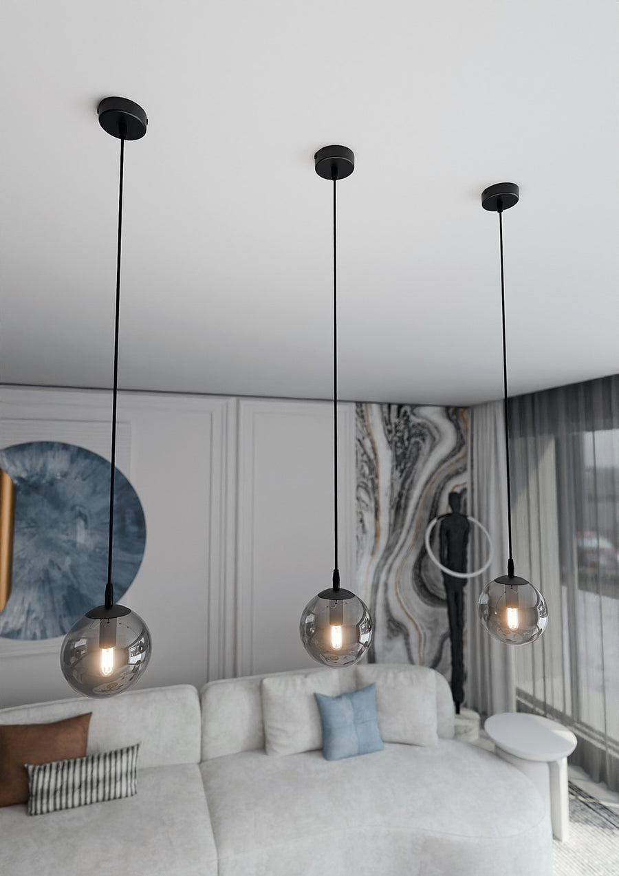 Vue en plongée de trois globes suspendus au plafond blanc, surplombant un canapé clair.