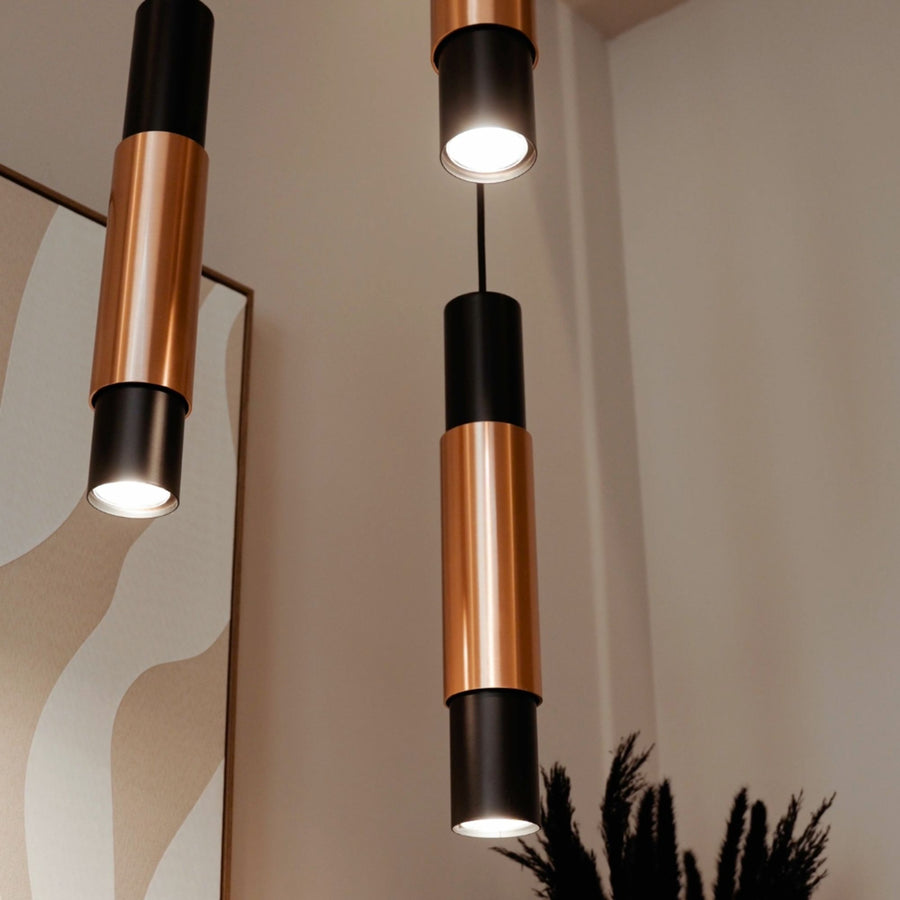 Détail de deux suspensions cylindriques noir et cuivre vues de dessous, lumière allumée.
