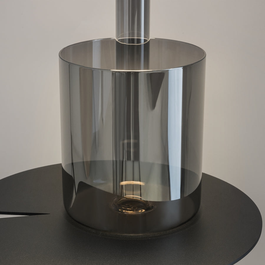 Détail du socle en verre fumé, reflets, base noire et source lumineuse interne.