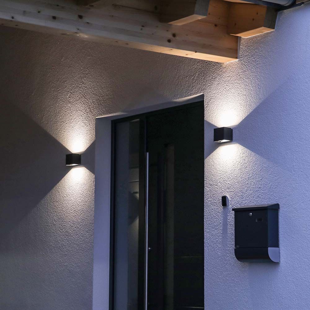 Entrée extérieure la nuit avec deux appliques noires encadrant une porte vitrée.