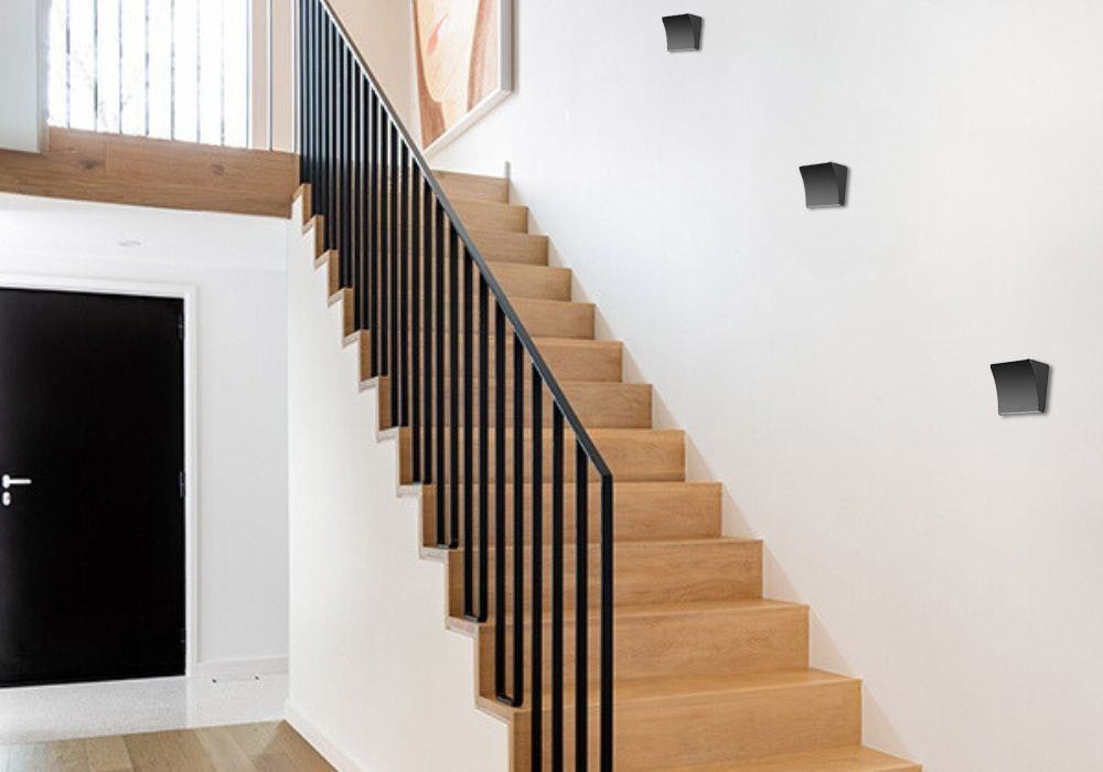 Mise en ambiance dans un escalier, plusieurs appliques murales noires fixées sur le mur.