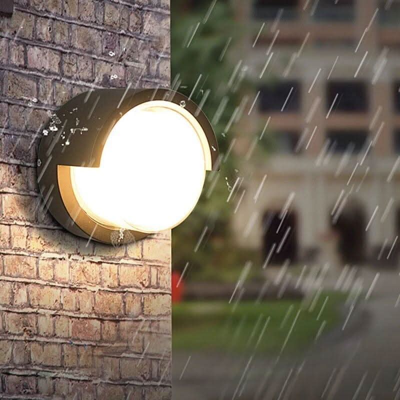 Vue rapprochée du luminaire mural sous la pluie, façade en briques et immeuble flou.