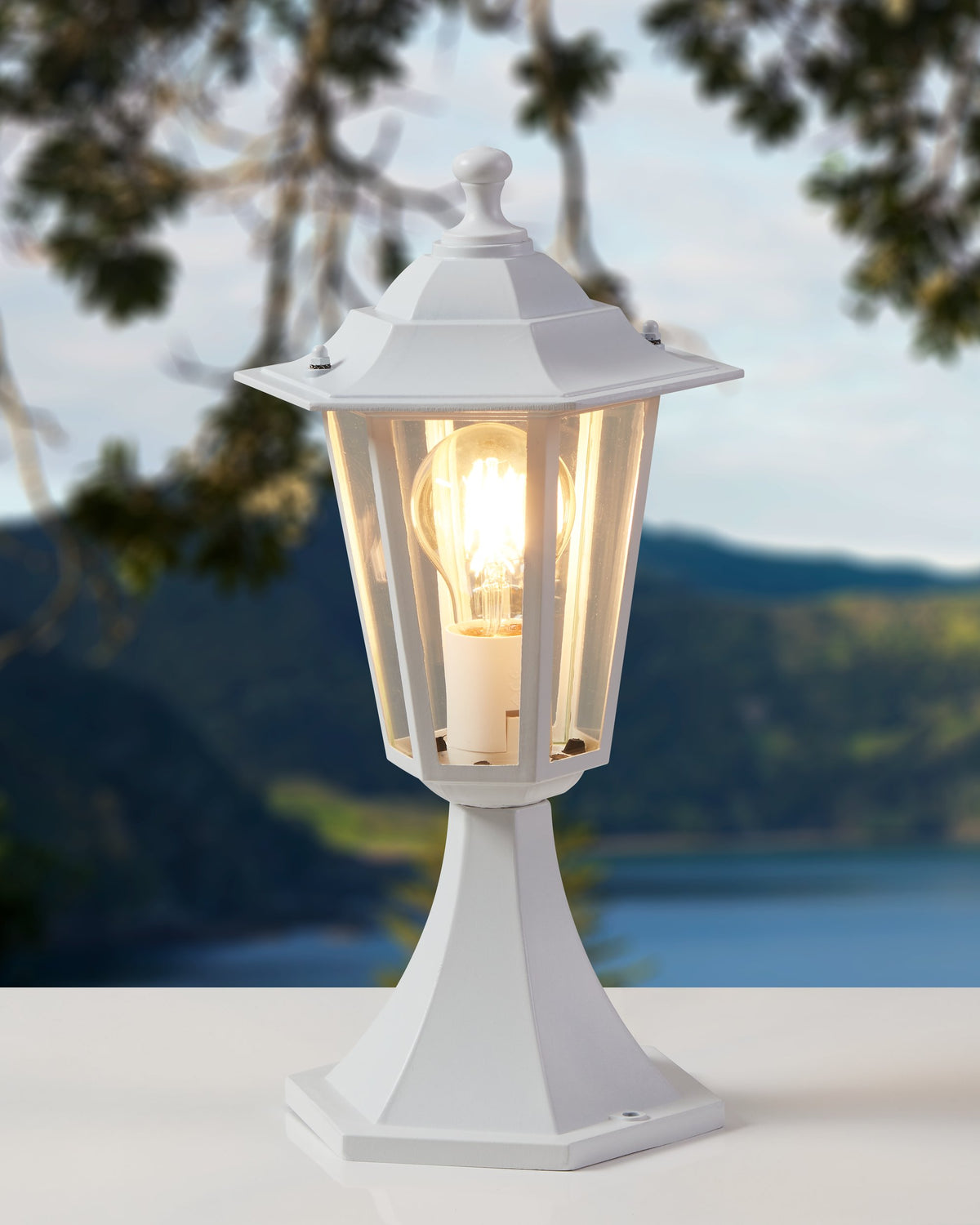 Lampadaire extérieur blanc allumé posé sur une terrasse, lac et montagnes en arrière-plan