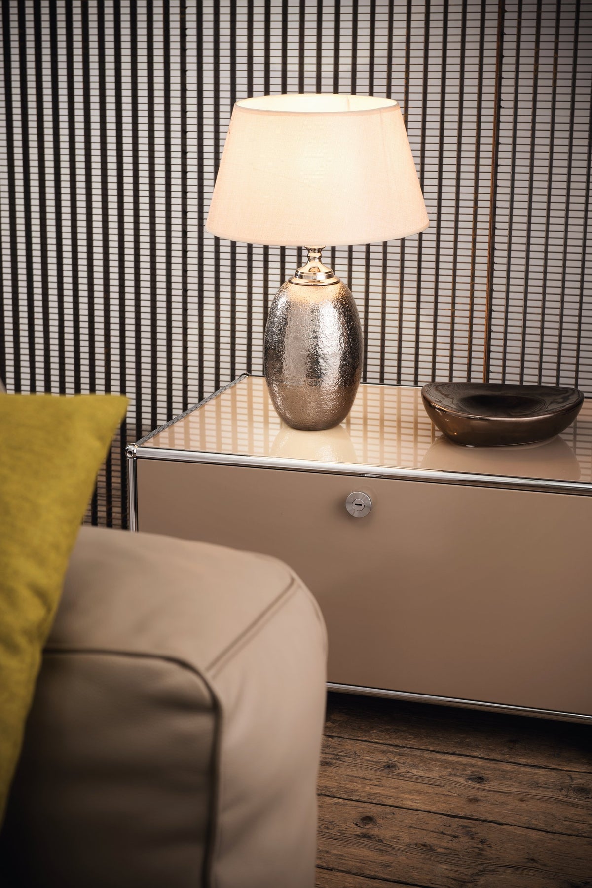 Lampe à poser allumée avec abat-jour blanc, posée sur un meuble, intérieur contemporain.