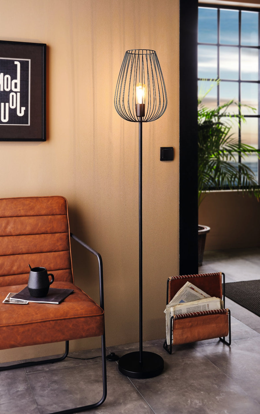 Lampadaire allumé dans un salon, fauteuil cuir et panier à journaux