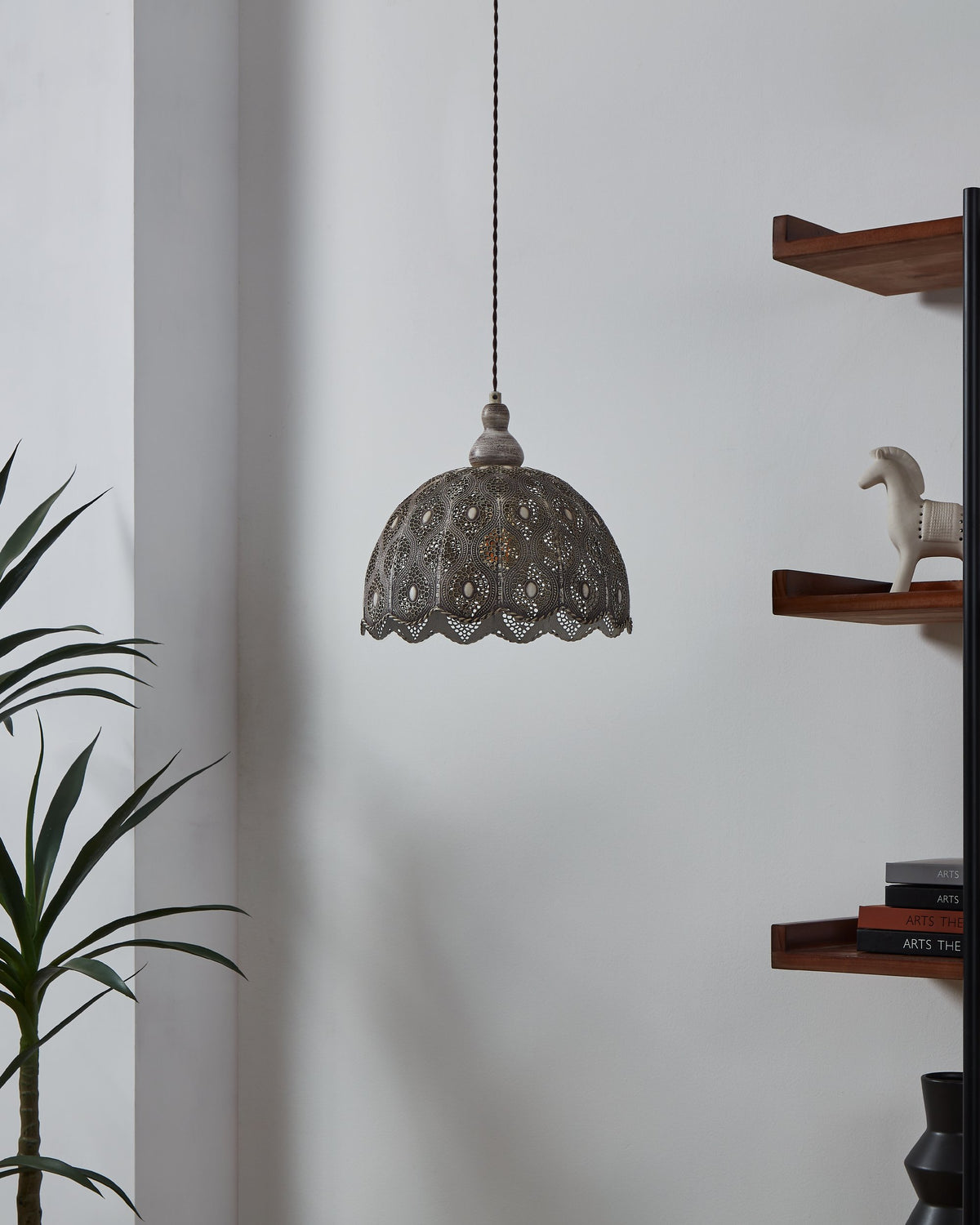Suspension éteinte dans un intérieur, ombre douce sur le mur et plante à gauche