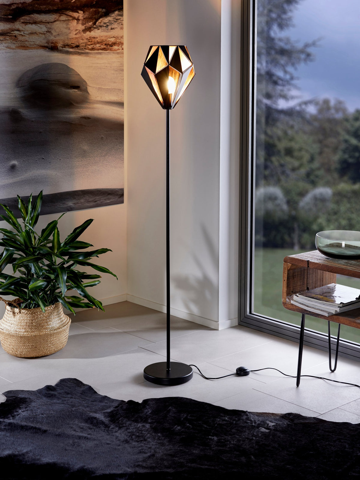 Lampadaire allumé dans un salon contemporain près d'une baie vitrée et d'une plante.