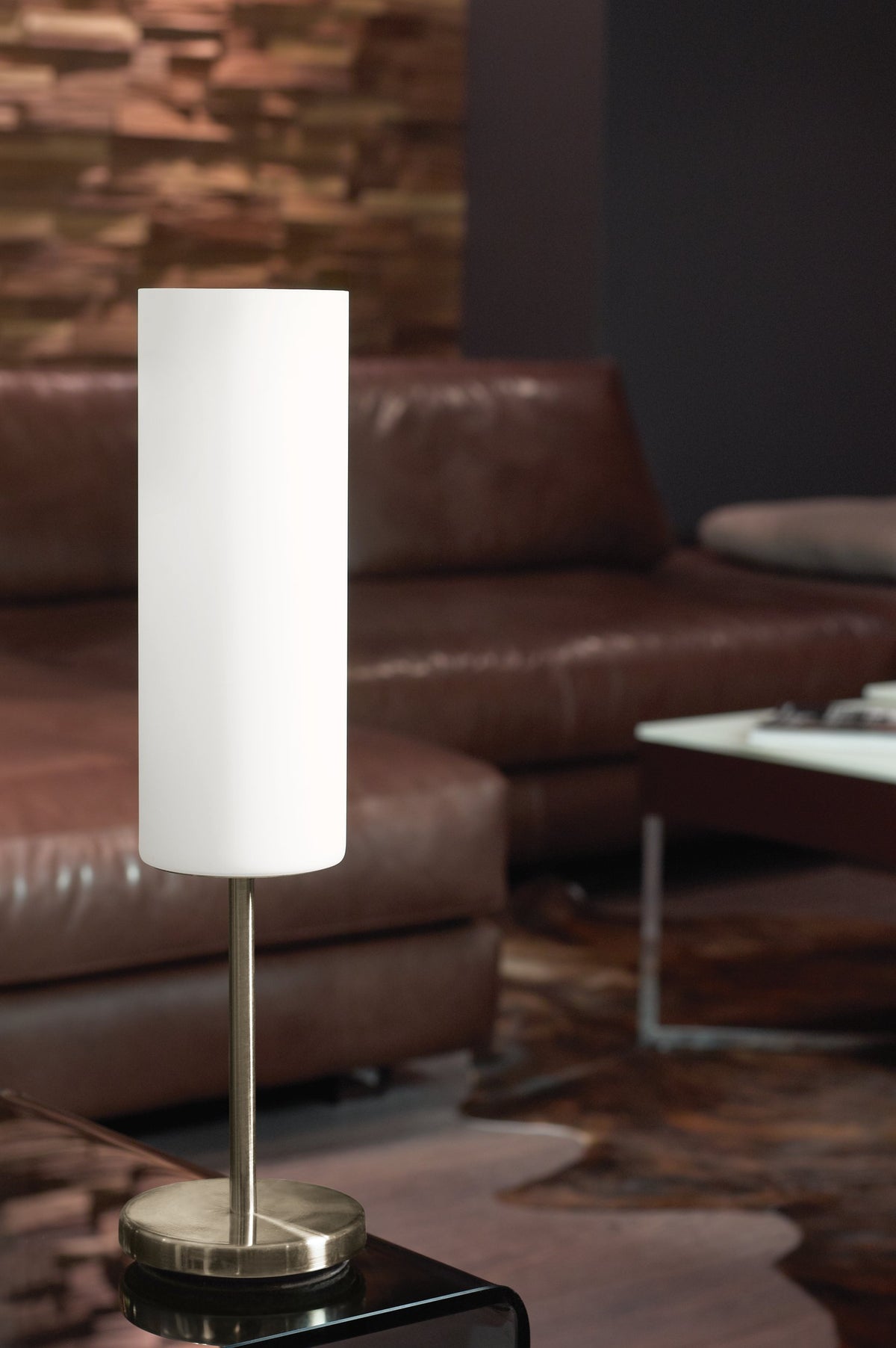 Lampe allumée posée sur table noire, canapé en cuir marron flou en arrière-plan