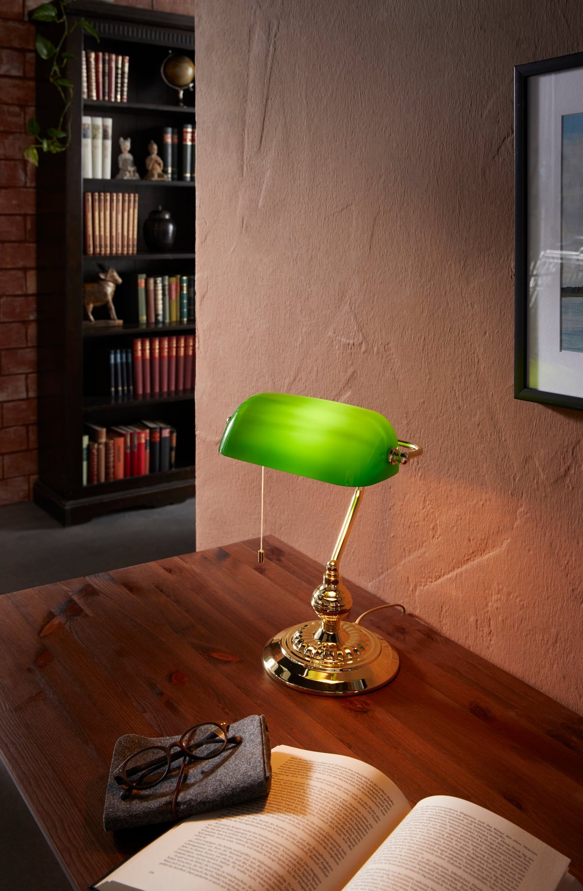 Mise en ambiance sur un bureau en bois, lampe allumée près d'un livre et de lunettes.