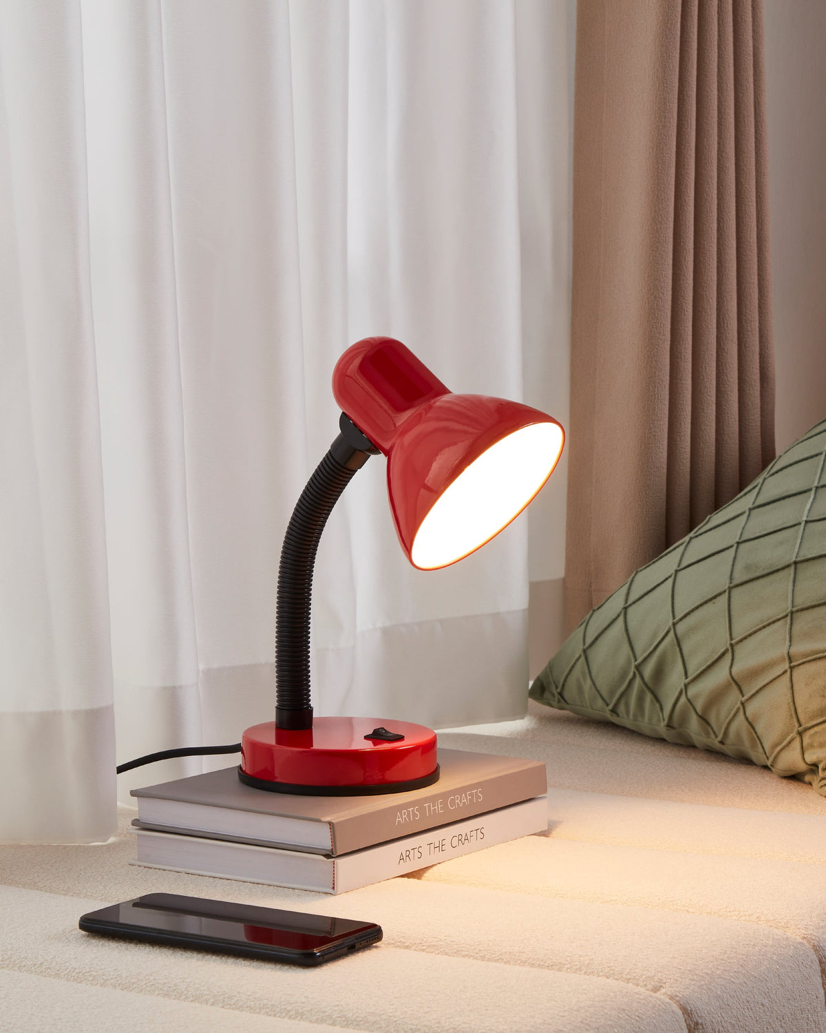 Mise en ambiance : lampe allumée posée sur deux livres au chevet d'un lit.