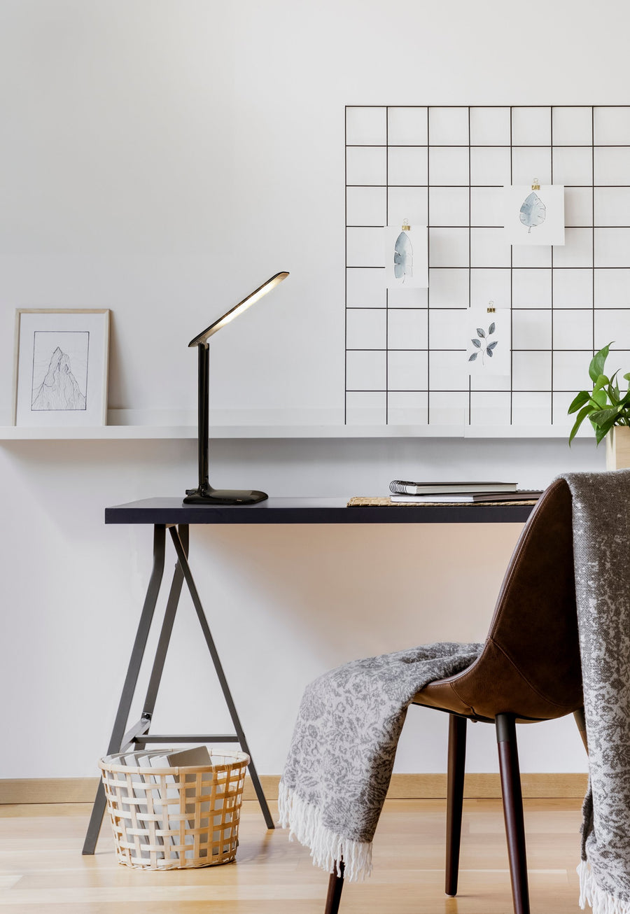 Lampe noire posée sur un bureau, mur quadrillé, fauteuil en cuir et panier