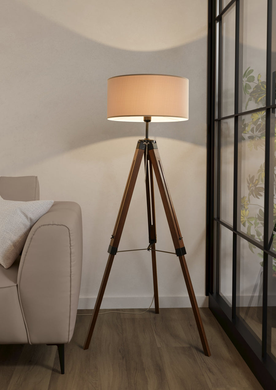 Lampadaire allumé placé près d'un canapé beige devant une grande verrière noire
