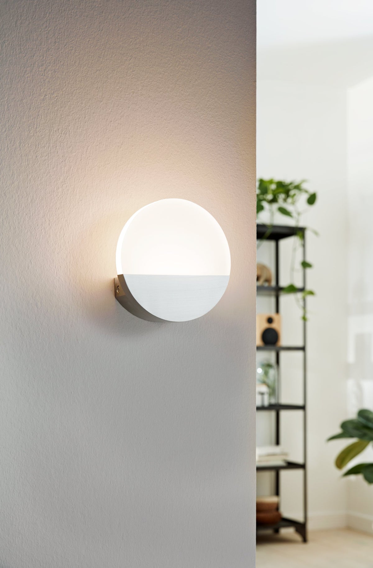 Mise en ambiance : applique ronde allumée diffusant une lumière chaude sur un mur intérieur