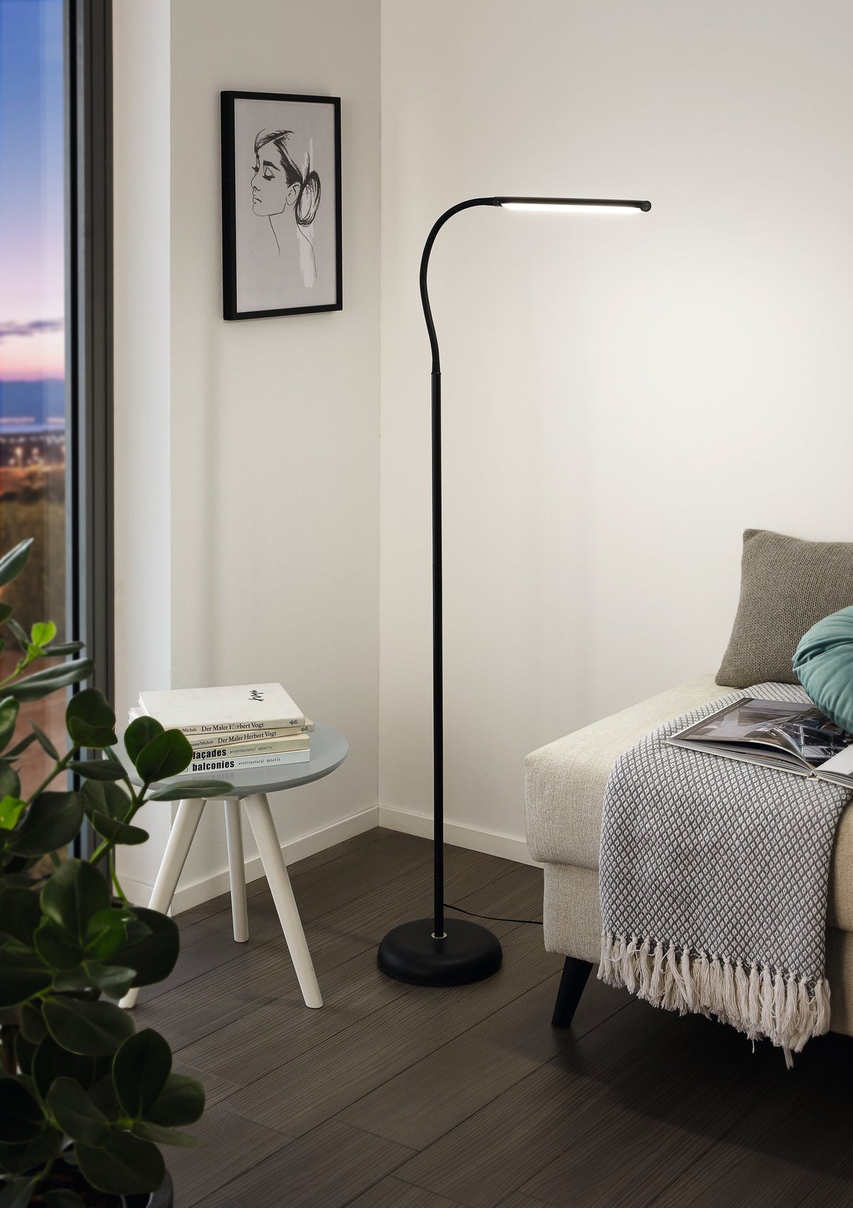 Lampadaire allumé dans un salon moderne, près d'un canapé, d'une table et d'une plante.