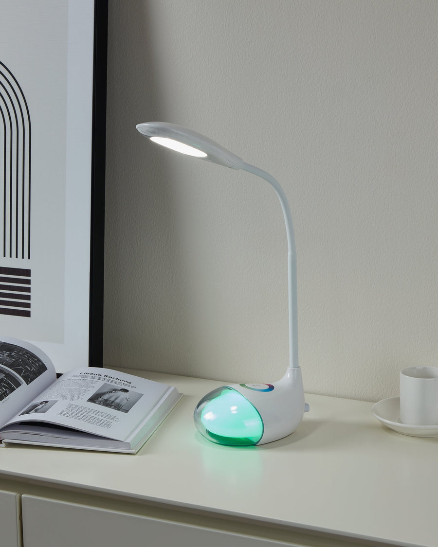 Lampe allumée posée sur un meuble blanc, socle diffusant une lumière verte près d'un livre ouvert.