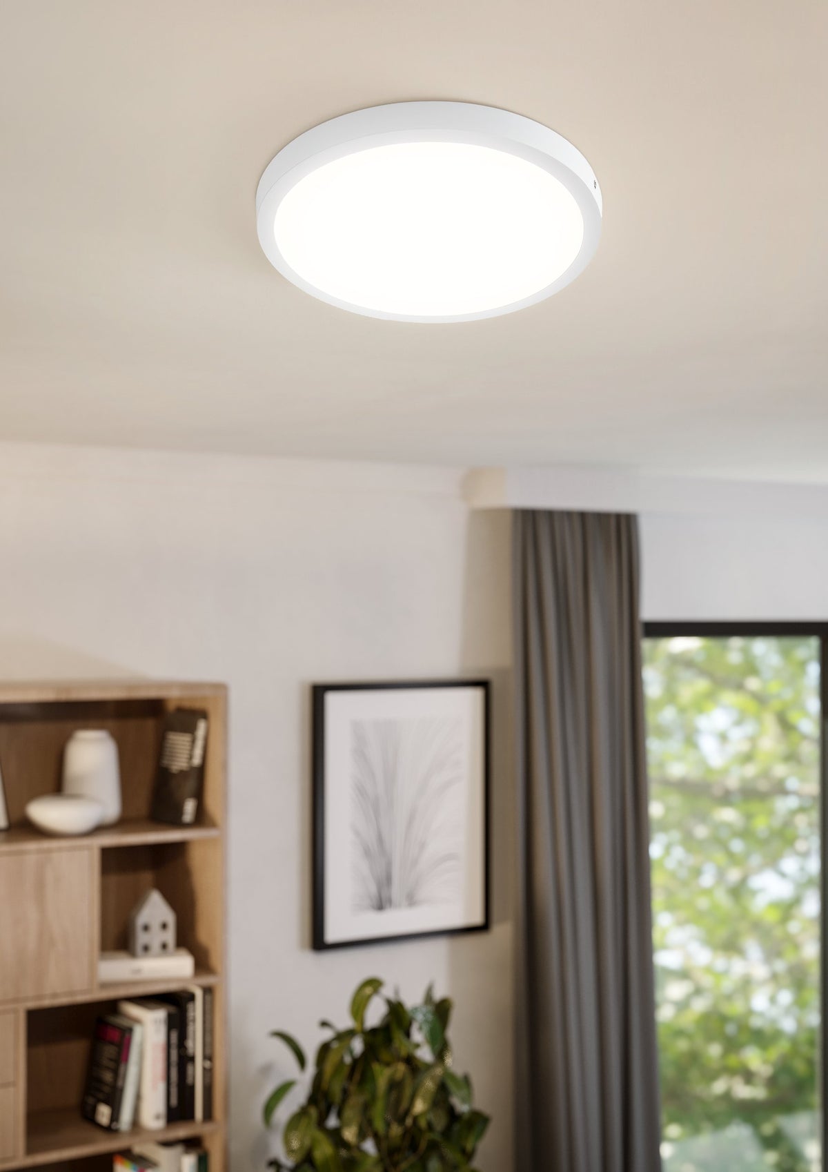 Mise en ambiance du plafonnier allumé dans un salon, étagère et cadre au mur