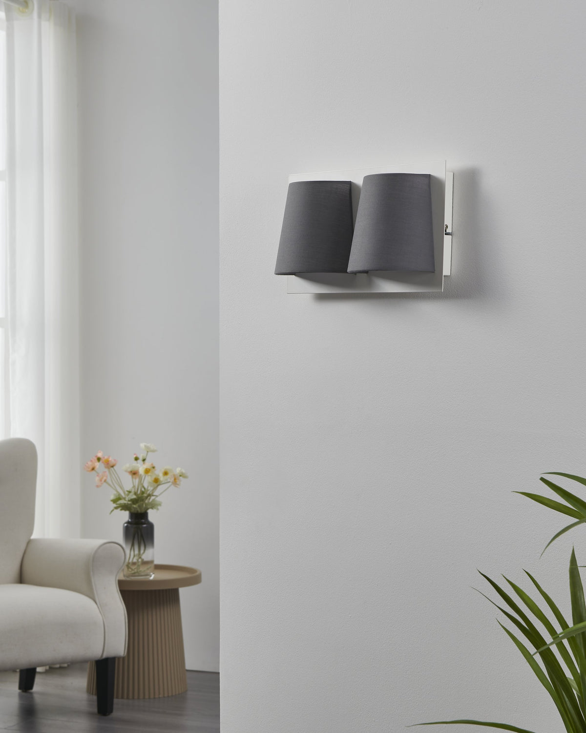 Luminaire mural gris installé dans un salon clair près d'un fauteuil
