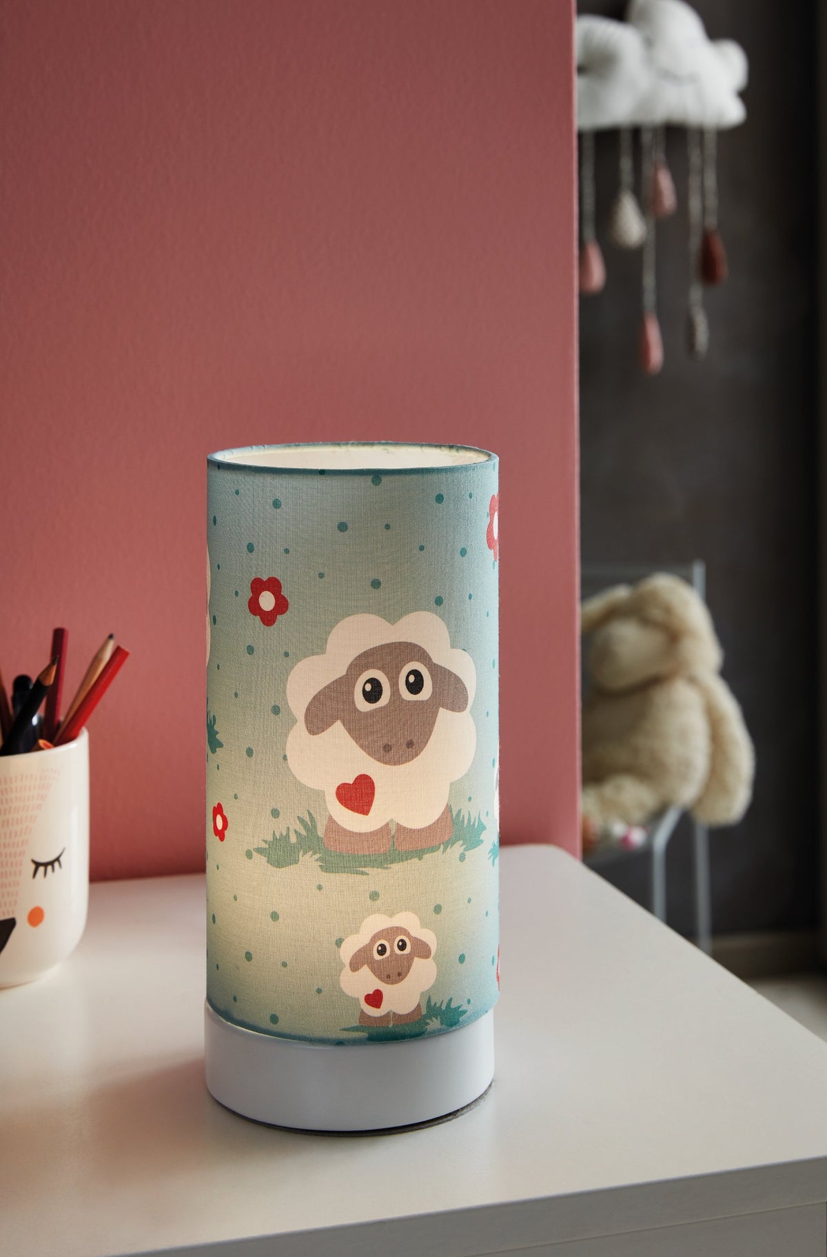 Lampe posée sur un bureau, ambiance chambre d'enfant, mur rose et pot à crayons.