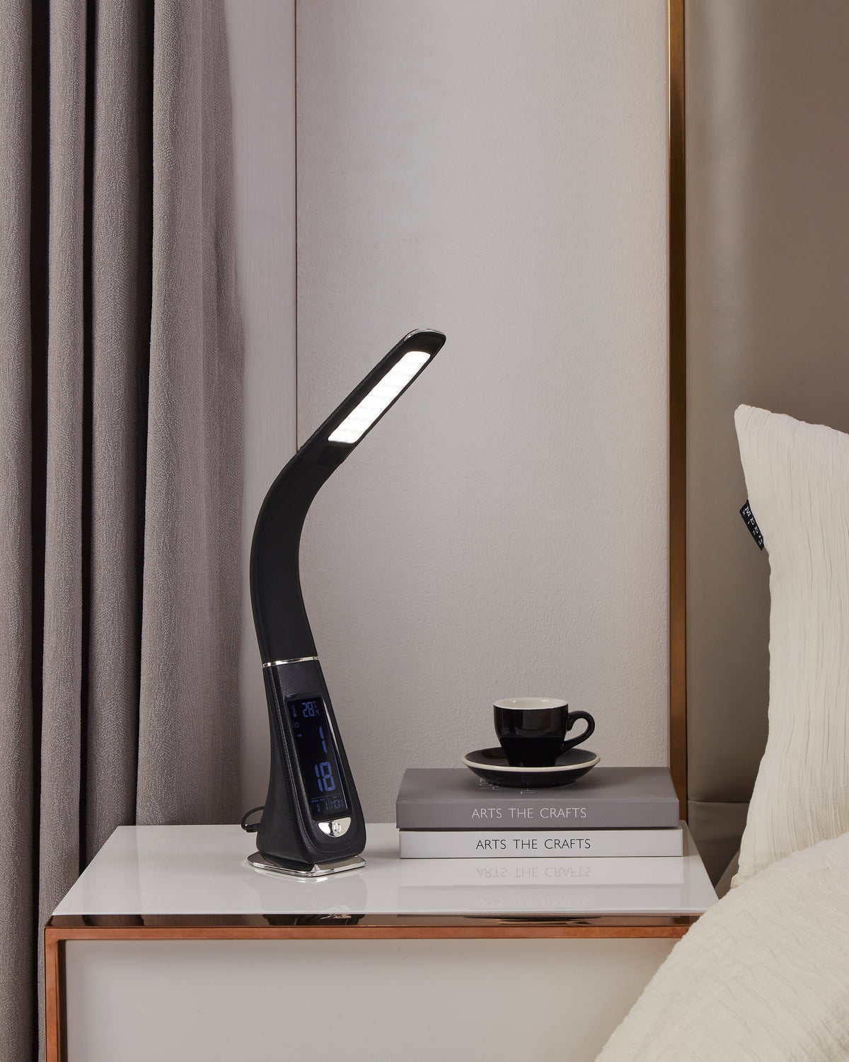 Ambiance chevet : lampe allumée près d'une tasse, de livres et d'un coussin blanc