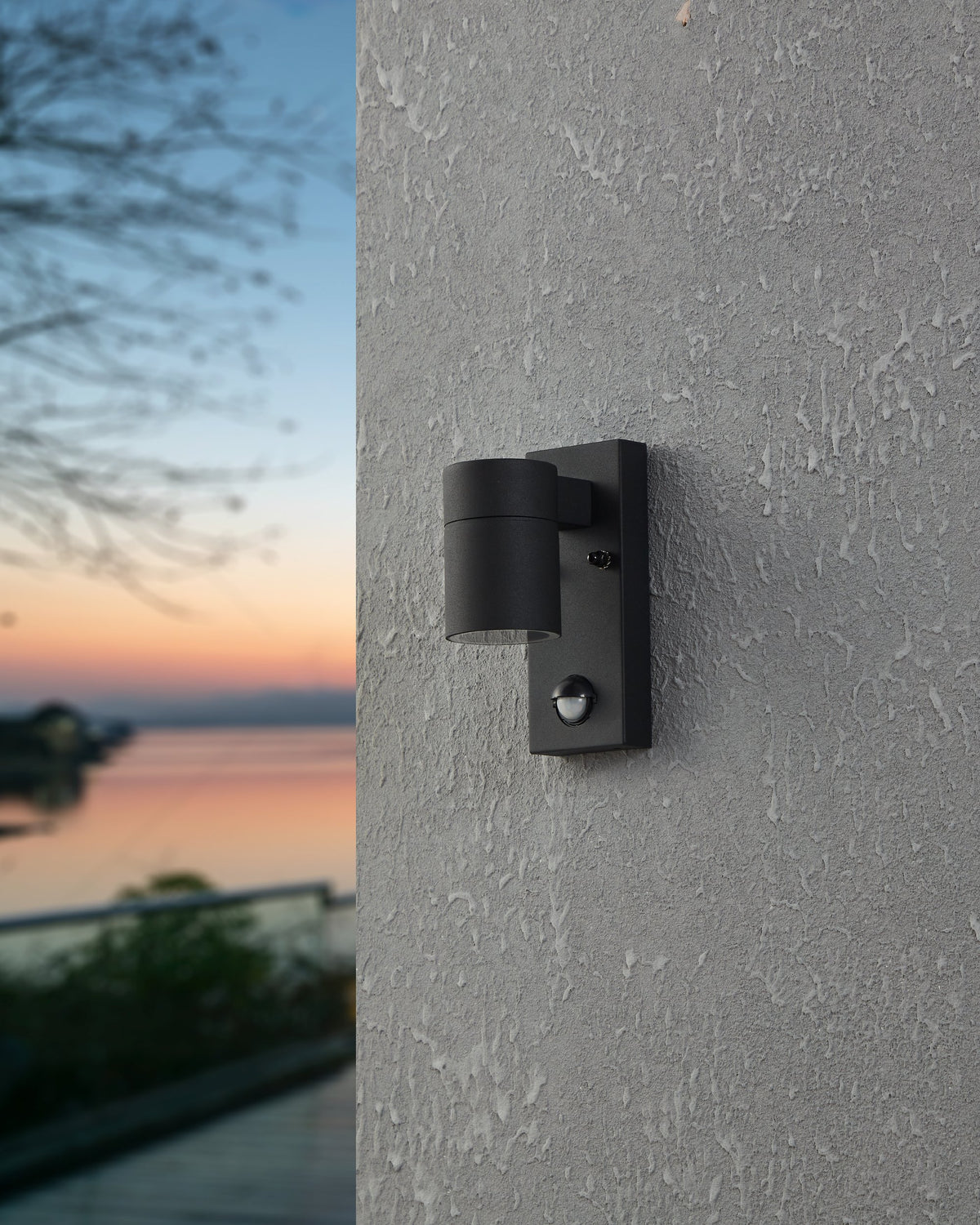 Même applique éteinte sur façade grise, paysage marin en arrière-plan flou