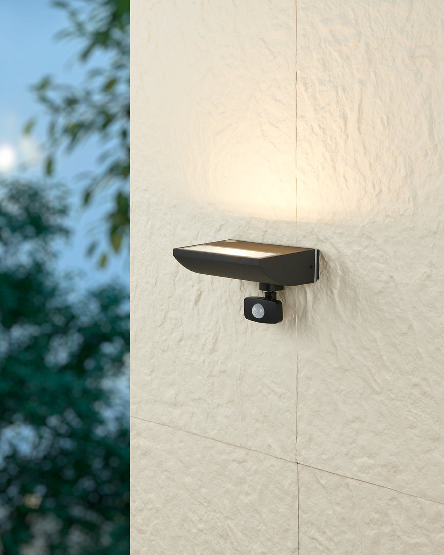 Vue de nuit du luminaire allumé projetant une lumière chaude sur un mur crépis