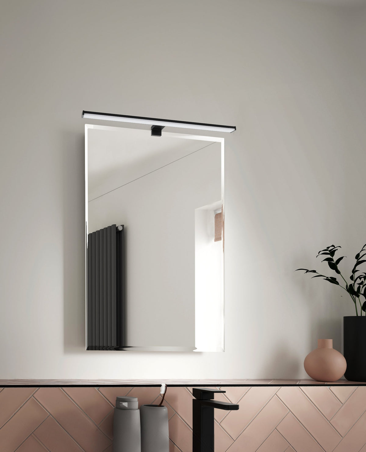 Vue en situation d'un luminaire mural au-dessus d'un miroir, carrelage rose en fond.
