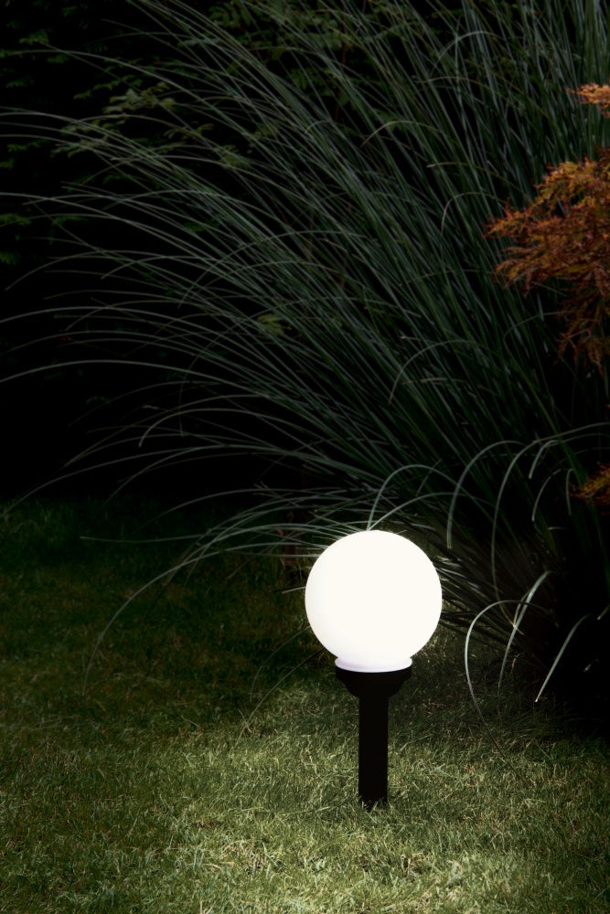 Luminaire boule allumé dans un jardin la nuit, parmi des graminées, mise en ambiance.