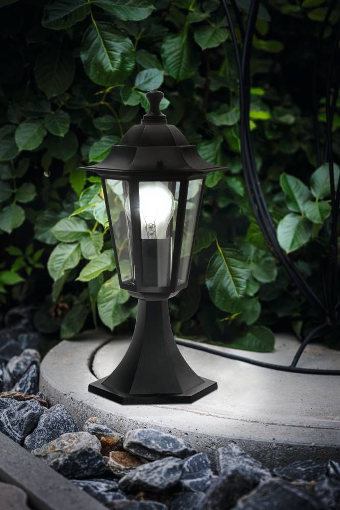 Mise en ambiance du lampadaire allumé dans un jardin, posé sur un muret près des feuillages