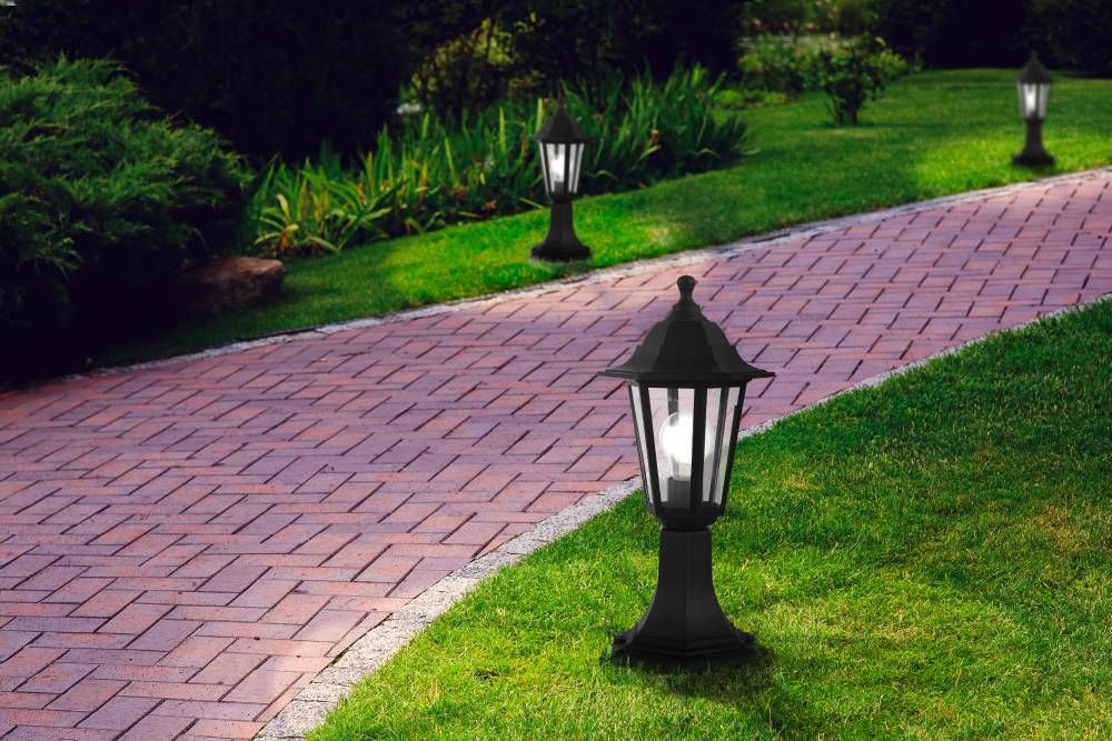 Trois lampadaires alignés le long d'une allée de briques rouges bordée de gazon vert