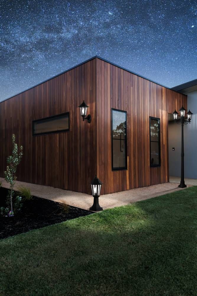Lampadaire allumé au pied d'une façade en bois, ciel étoilé en arrière-plan