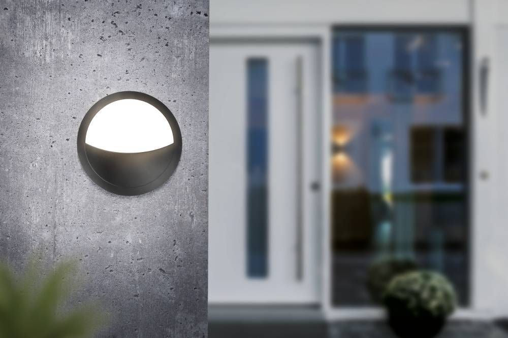 Applique ronde allumée fixée sur un mur béton devant une porte vitrée