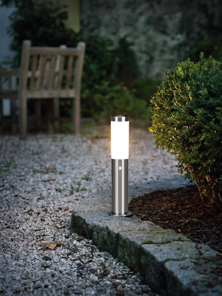 Lampadaire installé au sol dans un jardin, éclairant une bordure de graviers le soir