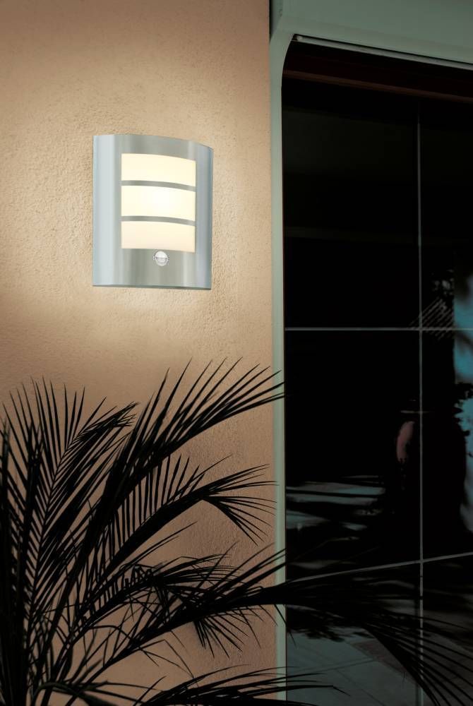 Vue de nuit du luminaire en fonctionnement sur un mur, proche d'une porte vitrée