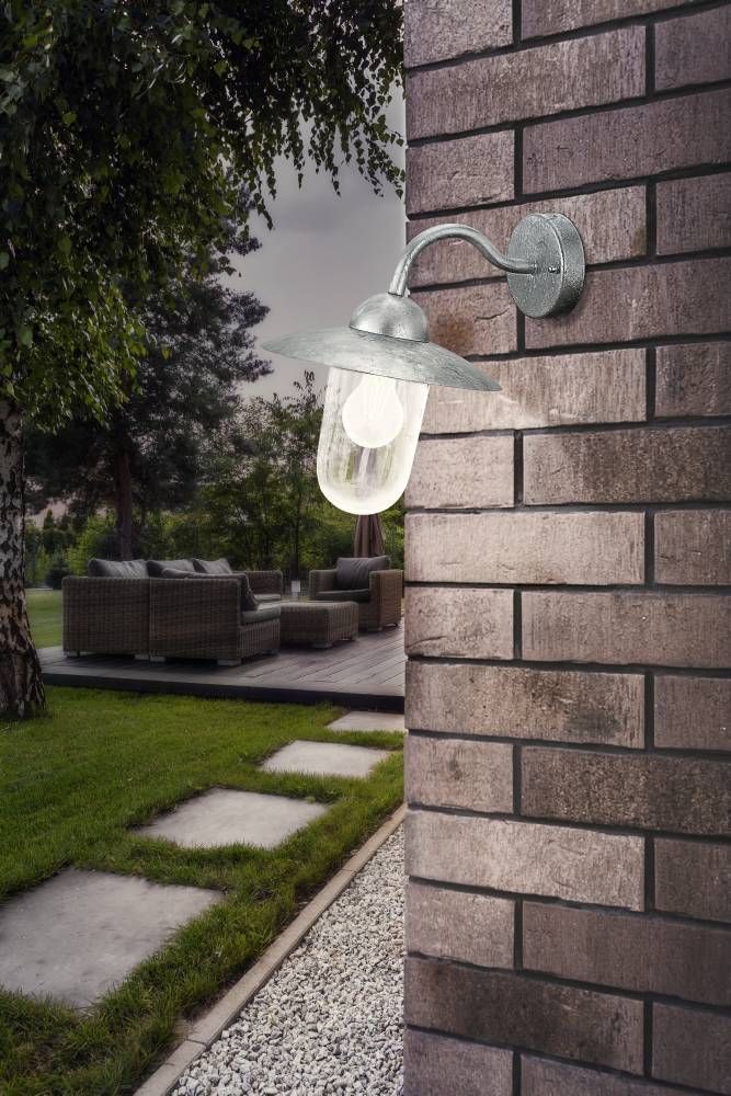 Luminaire mural allumé fixé sur un mur de briques, terrasse en bois et jardin