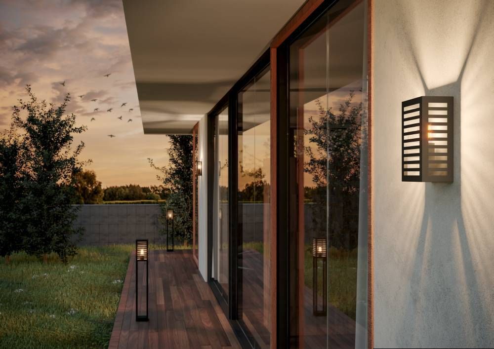Vue extérieure au coucher du soleil : applique murale allumée sur une terrasse en bois.