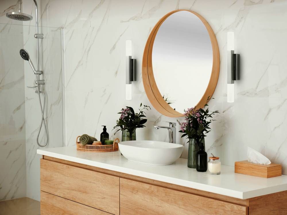 Ambiance salle de bain : deux appliques murales encadrent un miroir rond.