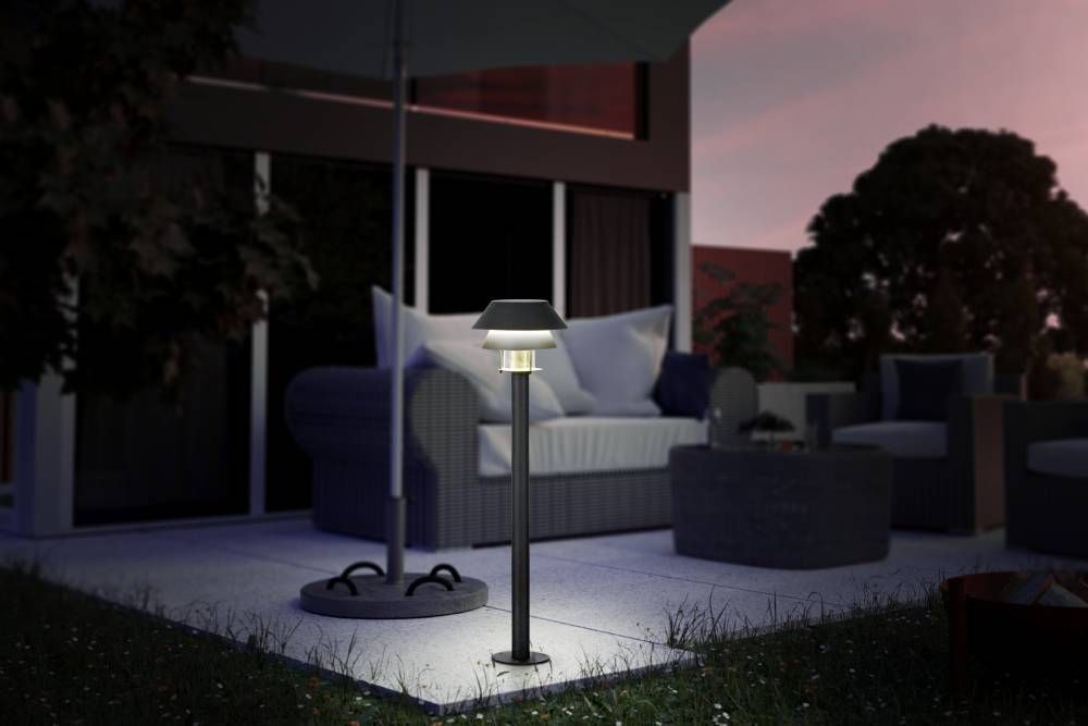 Lampadaire allumé sur une terrasse au crépuscule, près d'un canapé et d'un parasol.